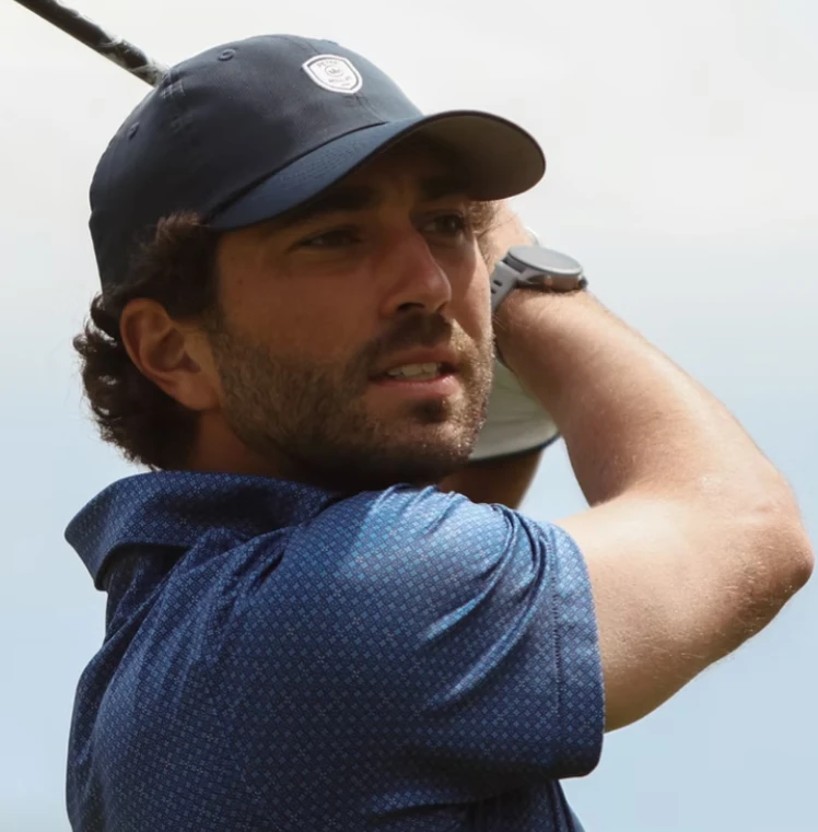 Joey Graziadei following through on a golf swing in a navy cap