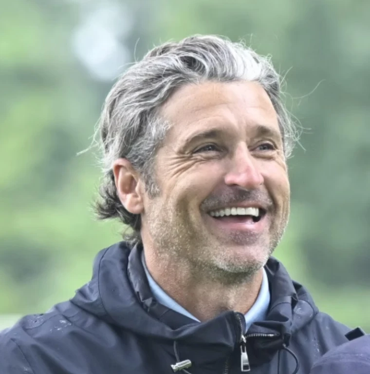 Patrick Dempsey, smiling outdoors in a navy jacket